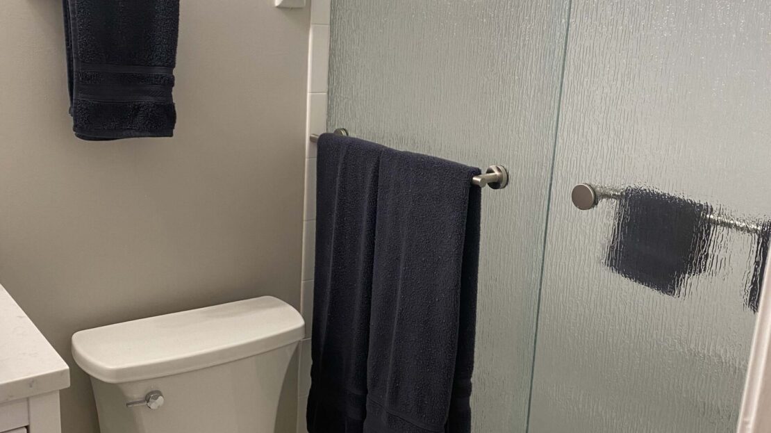 Clean bathroom with dark towels and glass shower door.