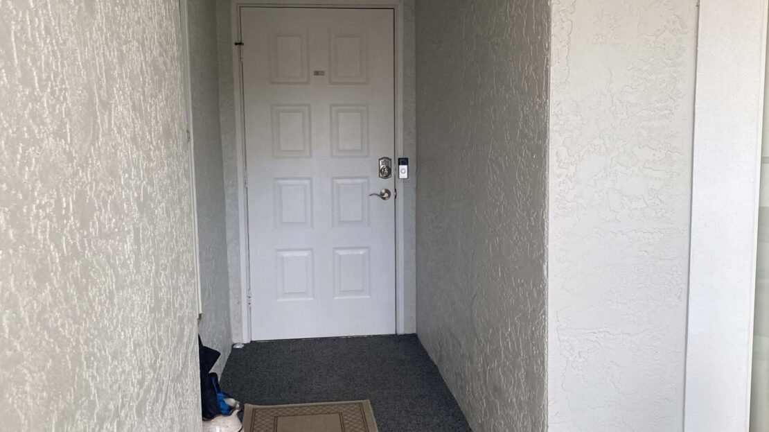 A white entrance hallway with a closed door and a doormat.