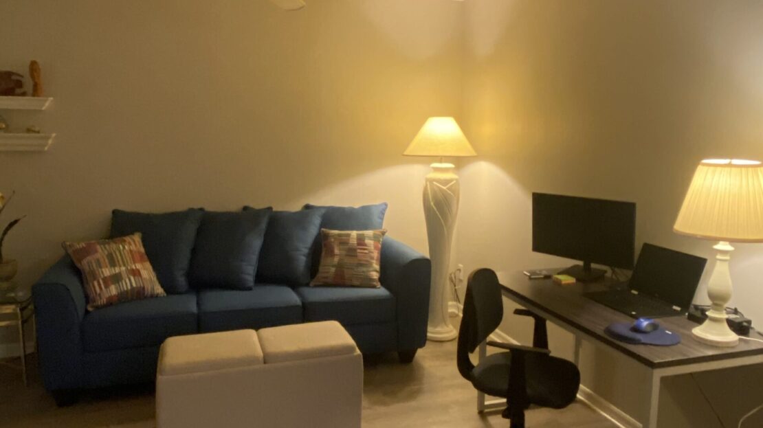 Cozy living room with blue sofa, ottoman, and computer desk setup.