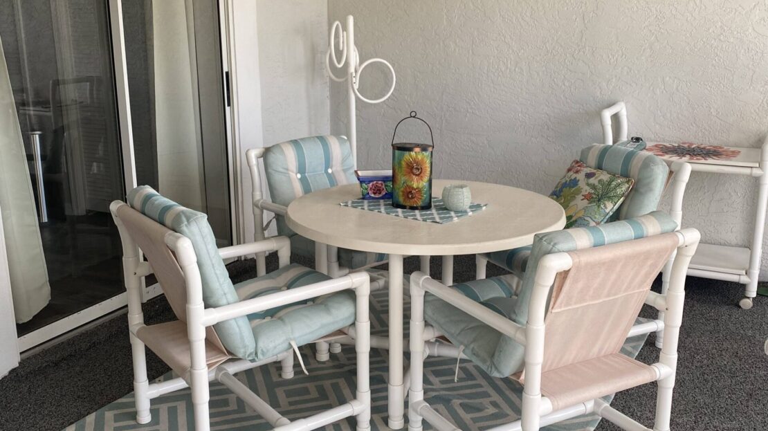 Outdoor patio set with a round glass table and four cushioned chairs on a patterned rug.