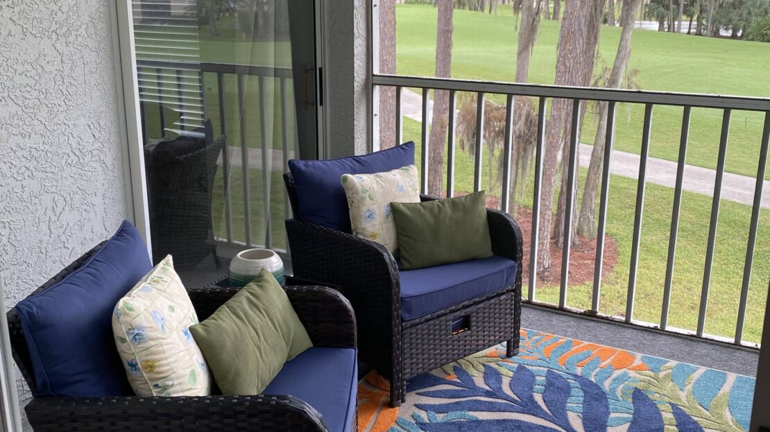 Cozy balcony seating with blue cushions and a colorful rug overlooking greenery.