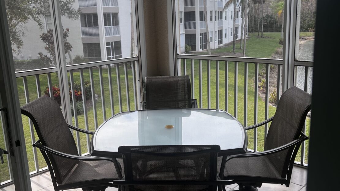Balcony dining set with glass table and four chairs overlooking a green courtyard.