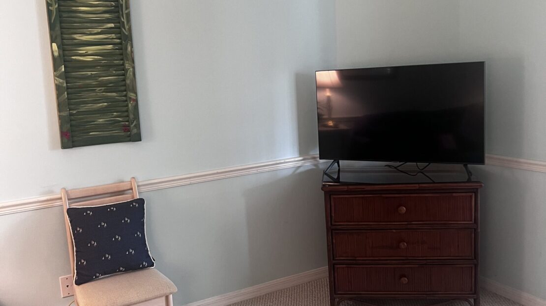 Minimalist room corner with TV on chest and chair.