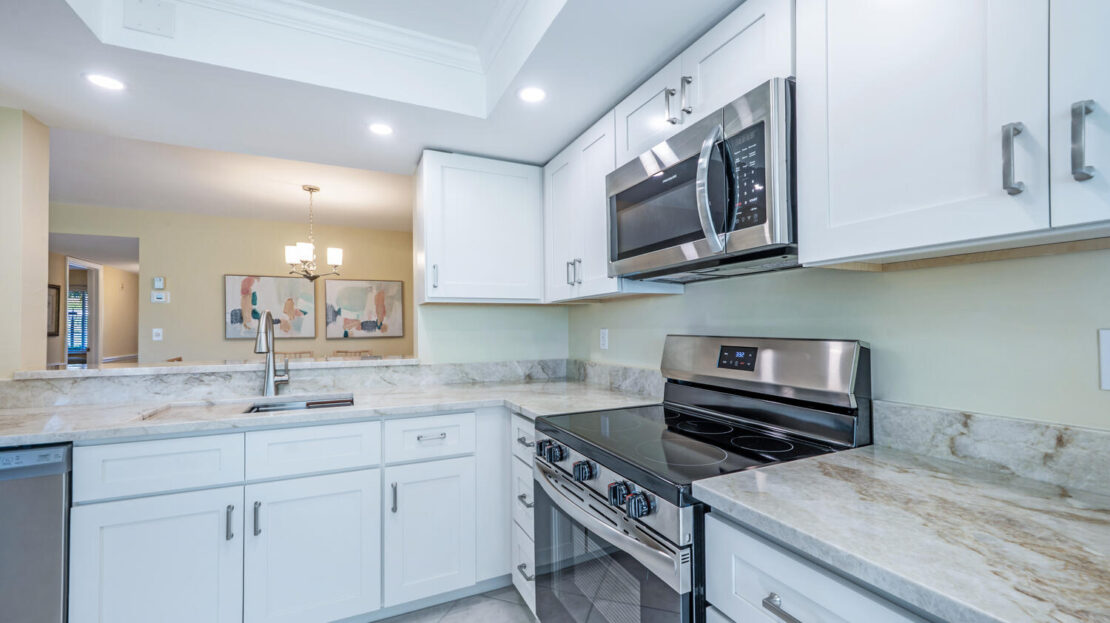 Modern white kitchen with stainless steel appliances and marble countertops.