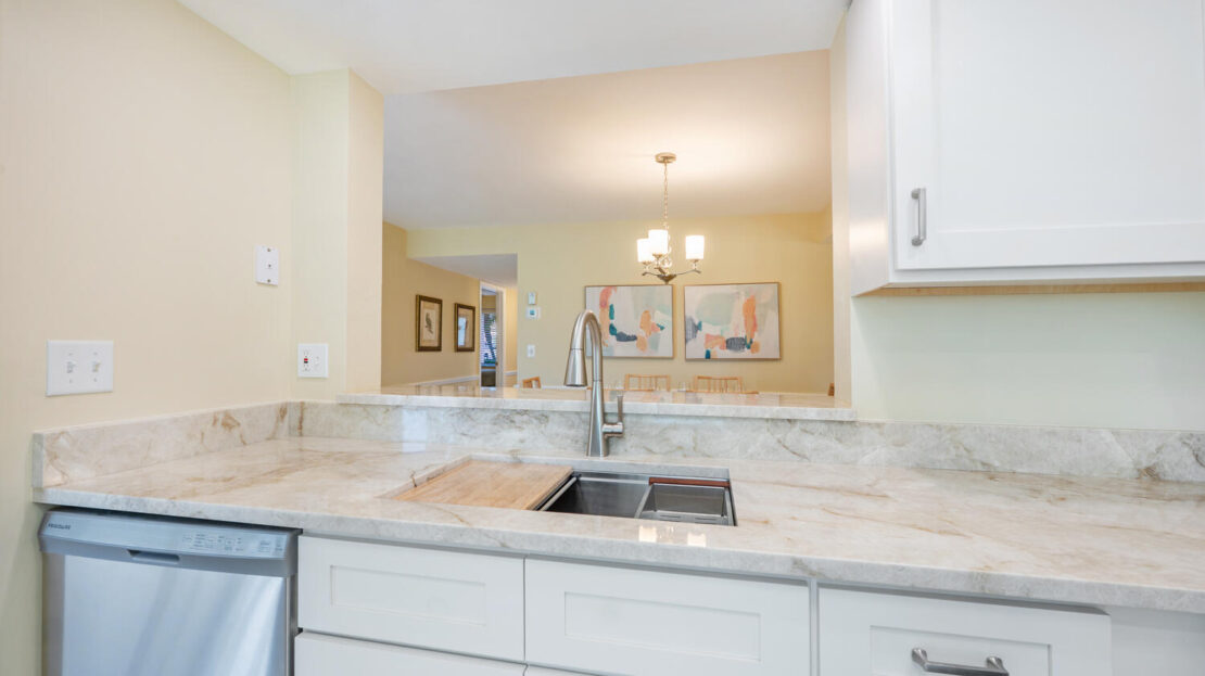 Modern kitchen sink area with marble countertop and white cabinetry.