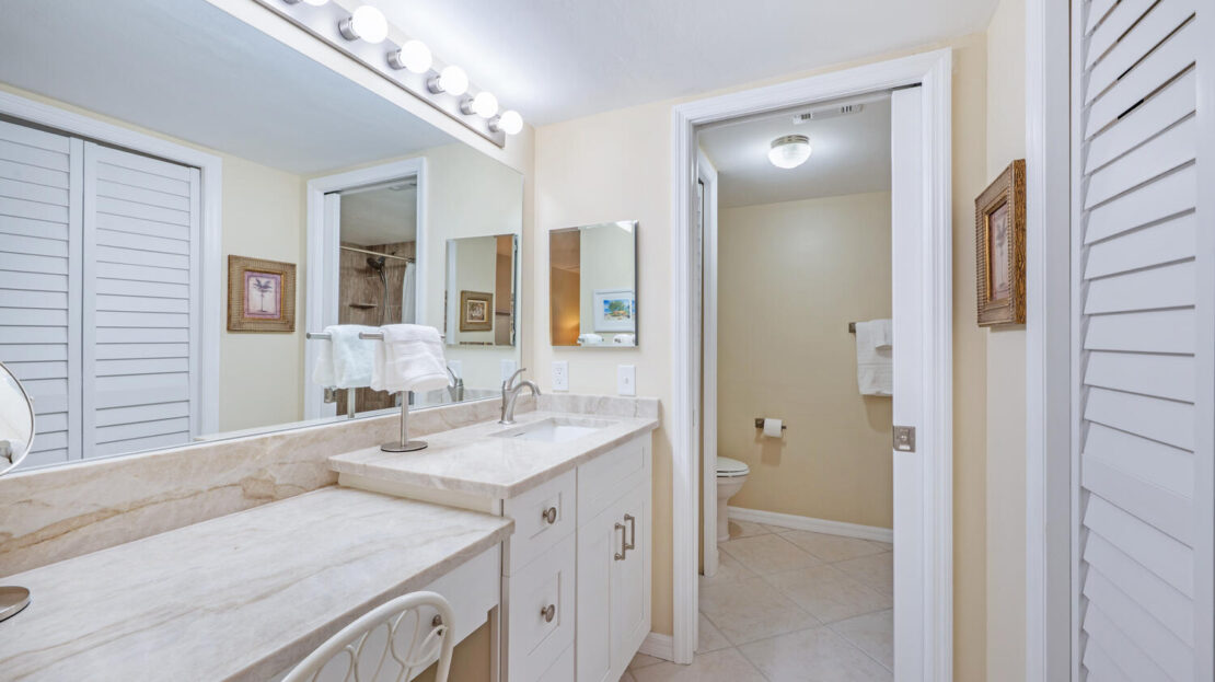 Bright bathroom with dual sinks and a separate toilet area.