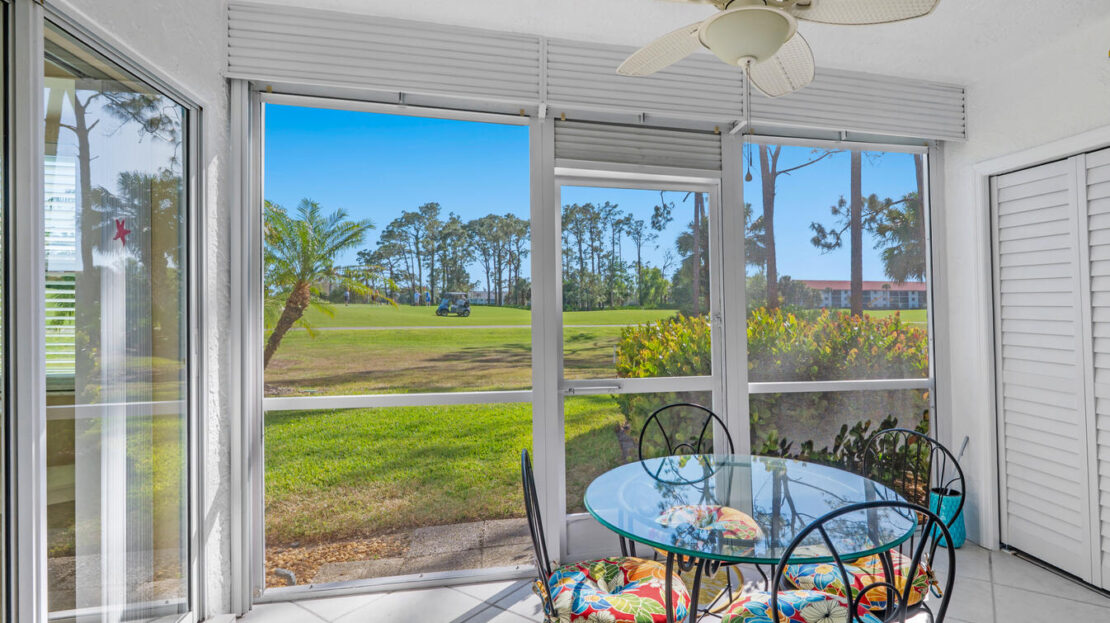 Bright sunroom with glass walls overlooking a green golf course.