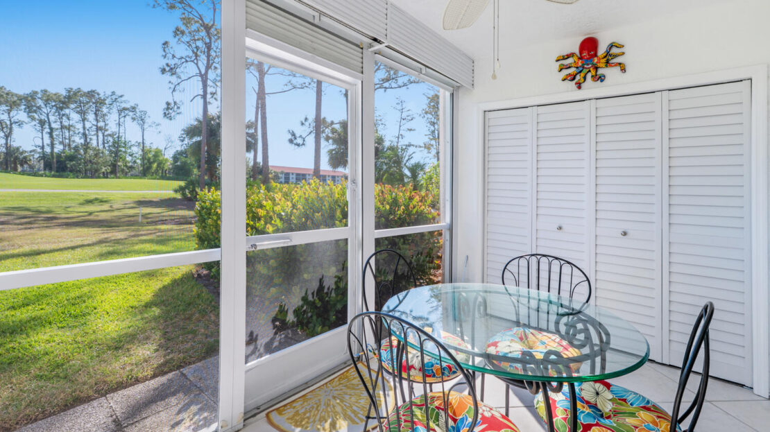 Bright sunroom with glass table and colorful chairs overlooking a garden.