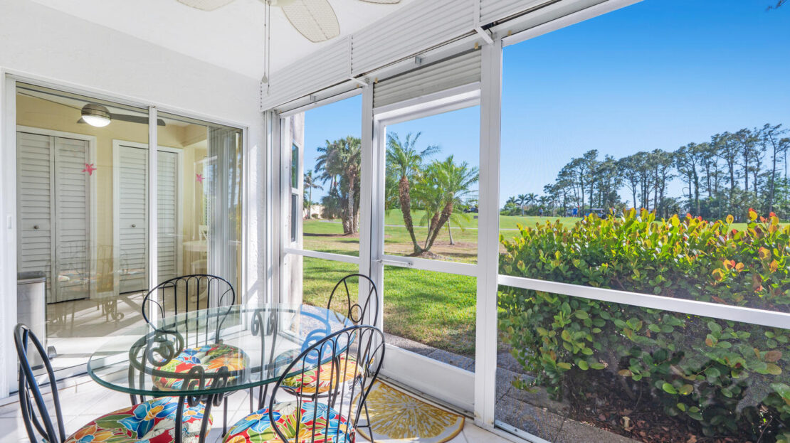 Bright sunroom with glass table and floral chairs overlooking a garden.