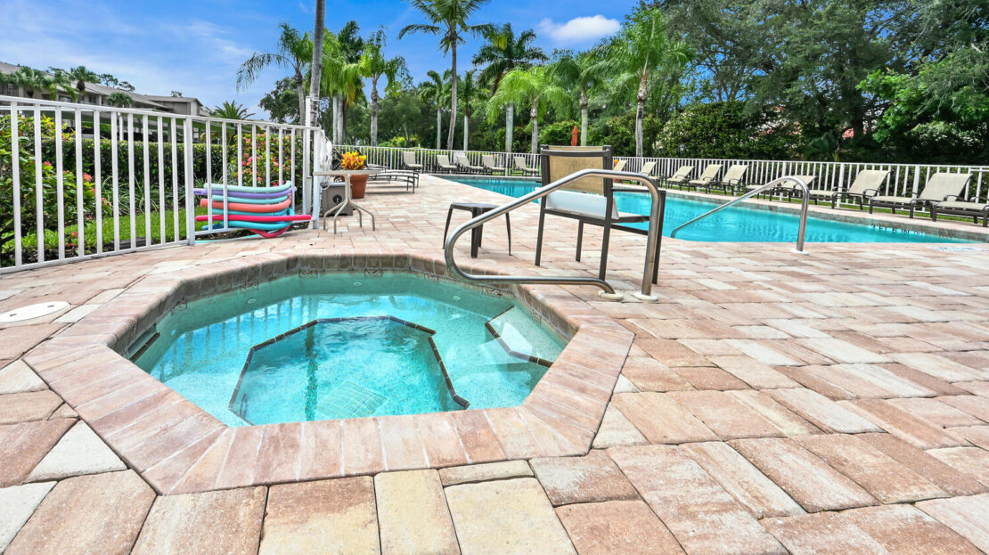 Outdoor pool area with a hot tub and palm trees under a clear blue sky.