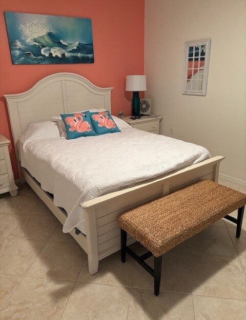 Cozy bedroom with white bed, floral pillows, and wicker bench.