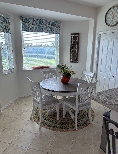 Cozy breakfast nook with white chairs and a round table by sunny windows.