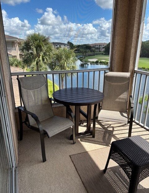 Balcony seating with two chairs and a table overlooking a lake and palm trees.