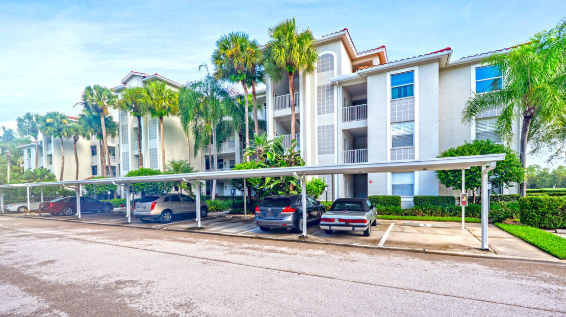Modern apartment complex with covered parking and palm trees under a clear blue sky.