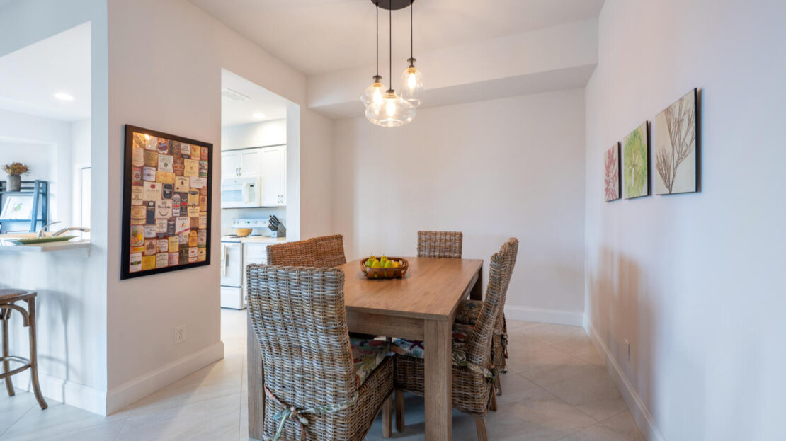 Modern dining room with wooden table and wicker chairs under hanging bulbs.