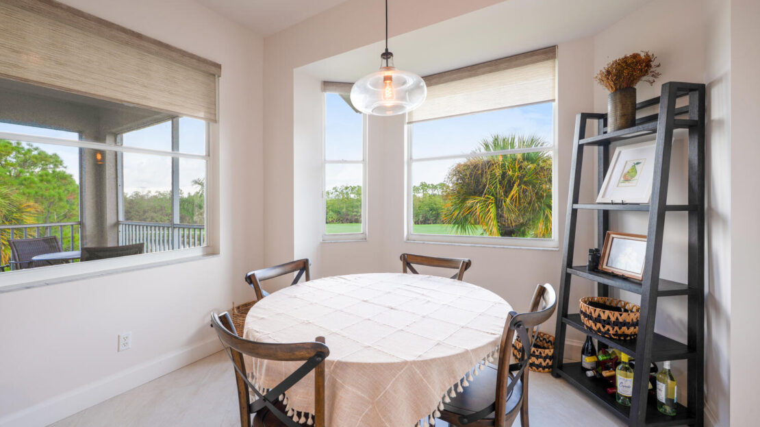Cozy dining area with round table and large windows overlooking greenery.
