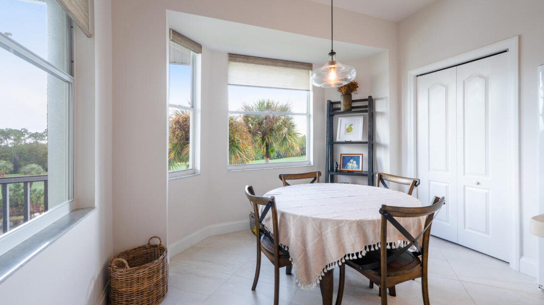Cozy dining nook with a round table and large bay window overlooking greenery.