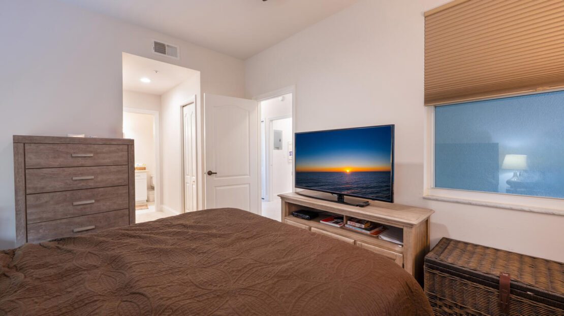Cozy bedroom with a TV showing a sunset over water.