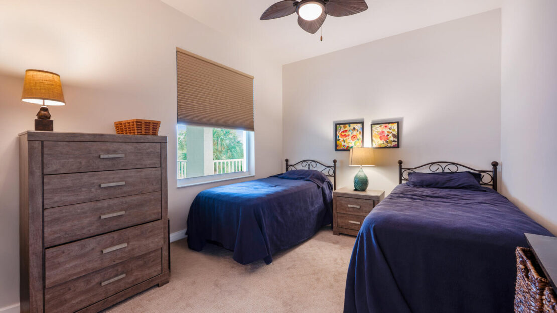 Cozy bedroom with twin beds, blue bedding, and soft lighting.