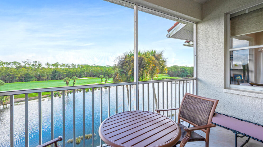 Balcony with round table and chairs overlooking a golf course under a blue sky.