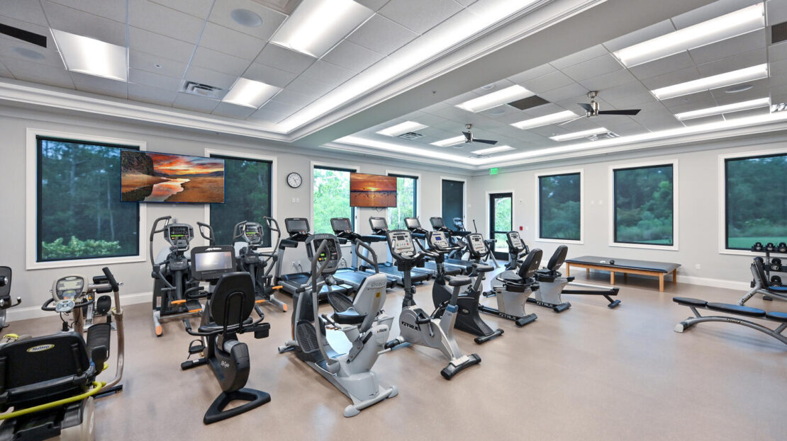 Modern gym room with cardio machines and large windows.