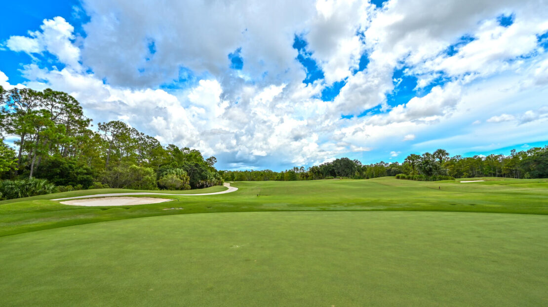 A lush golf course under a bright blue sky with scattered clouds.
