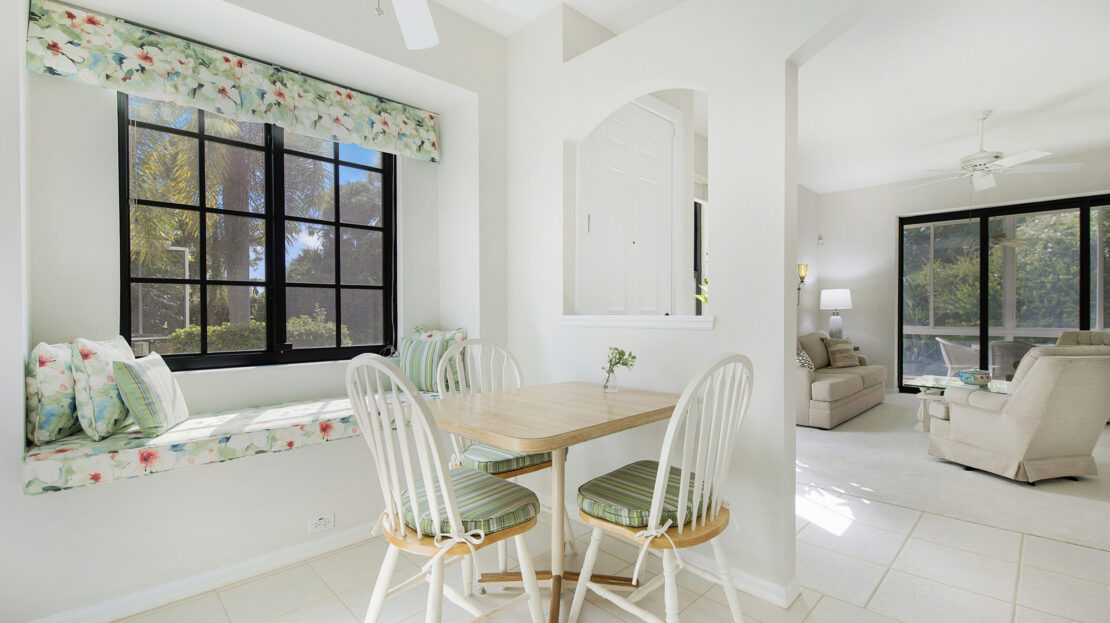 Bright dining area with white chairs and wooden table near large window.
