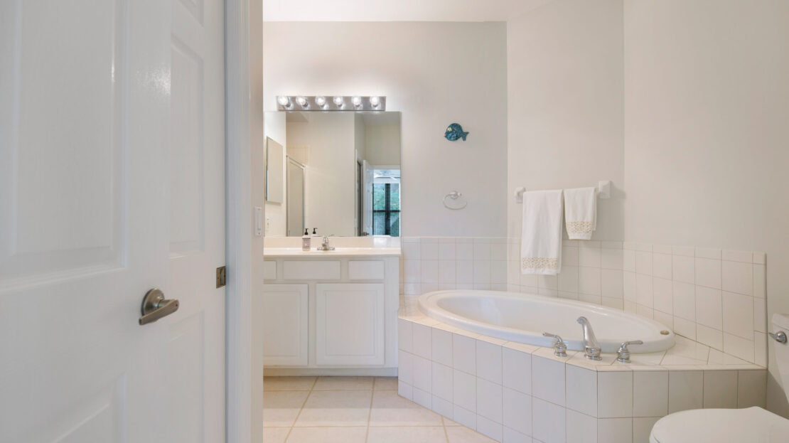 Bright bathroom with white tiles, a bathtub, and a vanity mirror with lights.