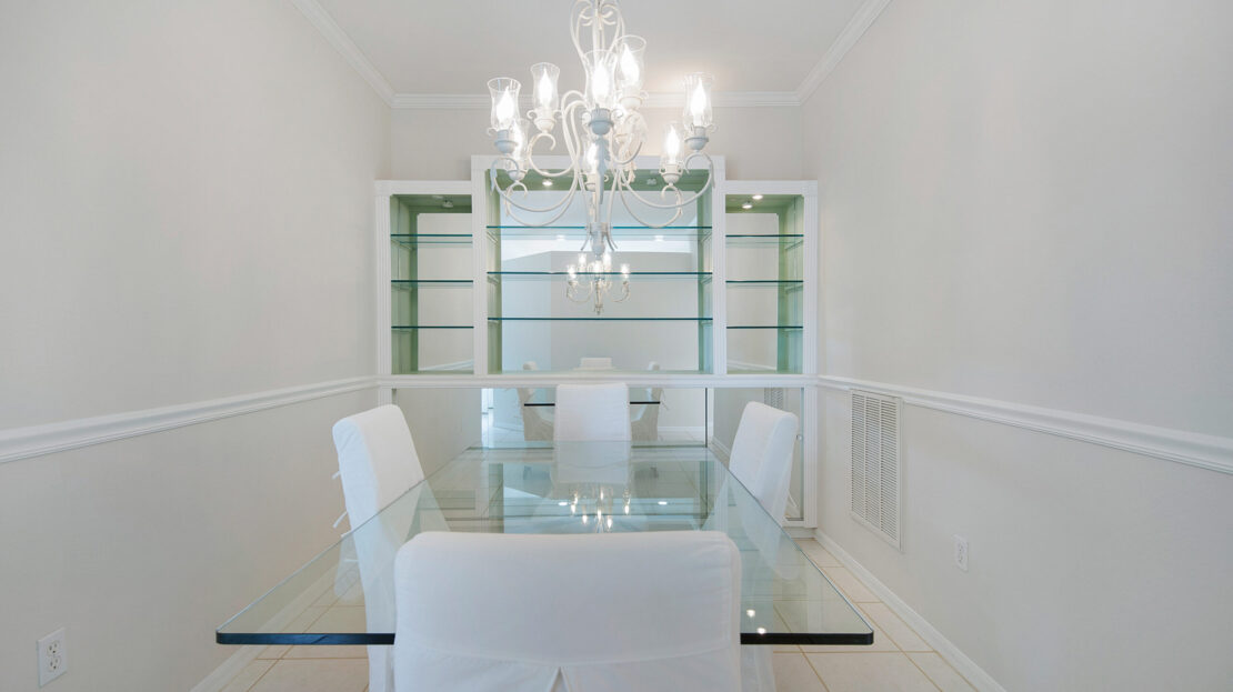 Modern dining room with white chairs and glass table under chandelier.