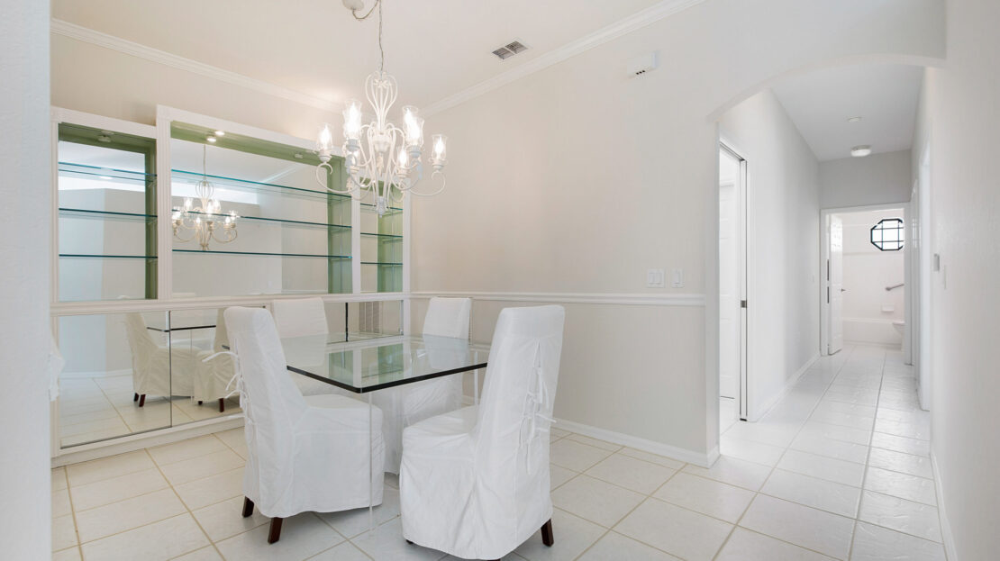 Elegant dining area with glass table and white upholstered chairs under chandelier lighting.