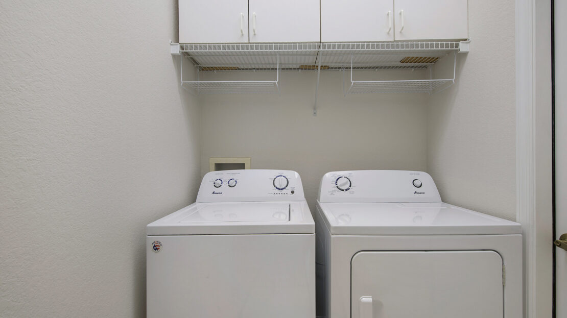 A clean laundry room with a washing machine and dryer beneath white cabinets.