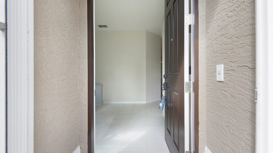 Empty room with an open dark wooden door and tiled floor.