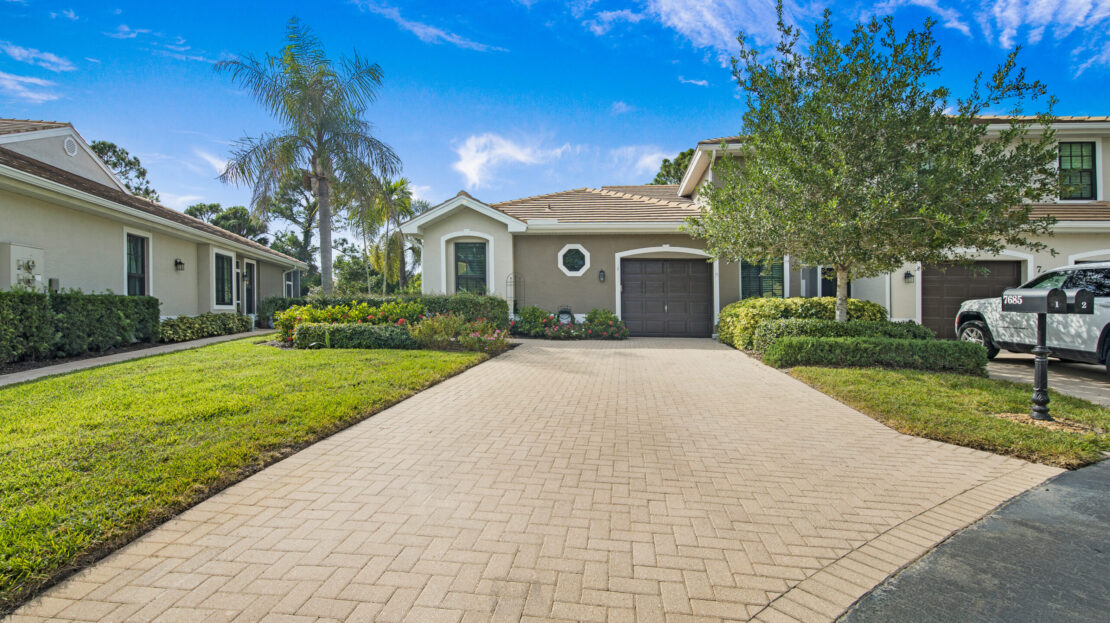 Single-story house with a paved driveway and attached garage under a blue sky.