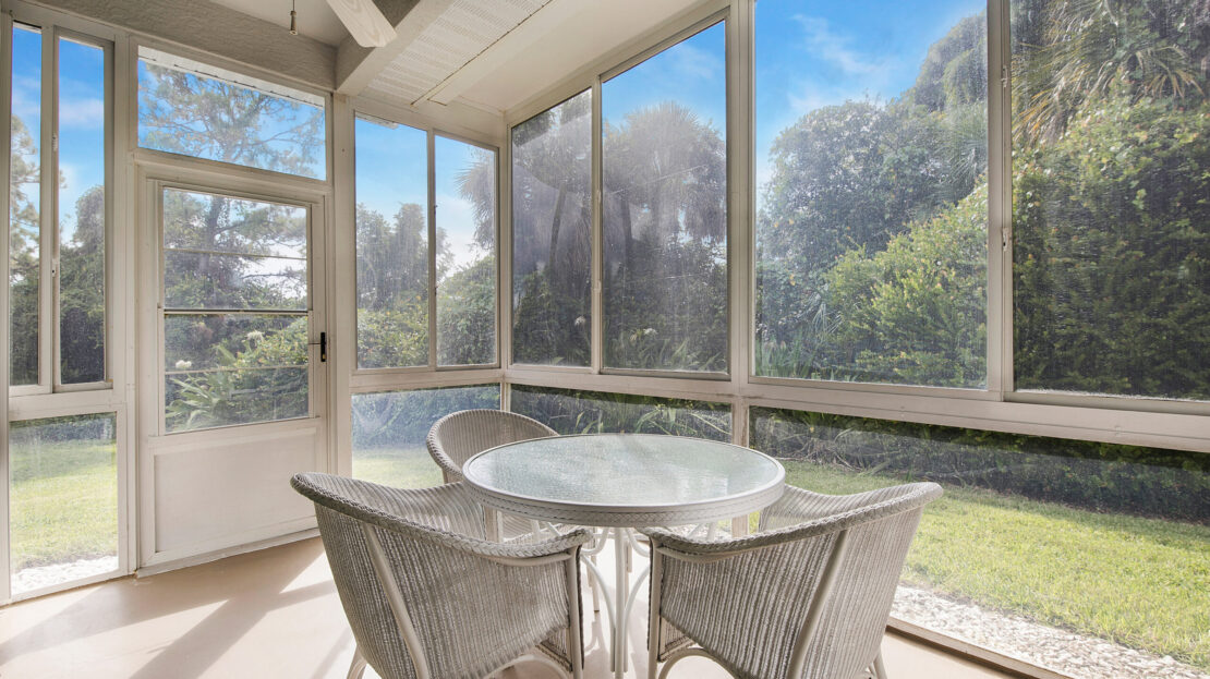 Cozy sunroom with round table and wicker chairs overlooking greenery.