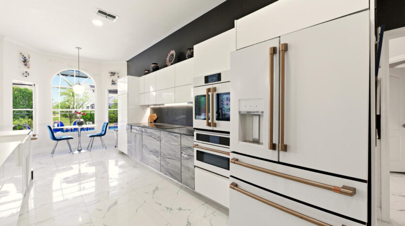 Modern white kitchen with sleek appliances and marble flooring.