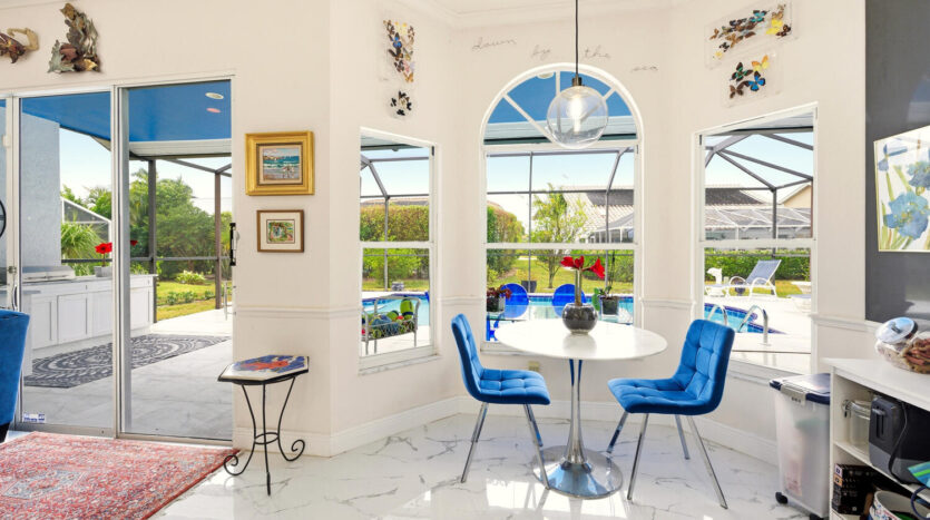 Bright dining area with blue chairs and large windows overlooking the pool.