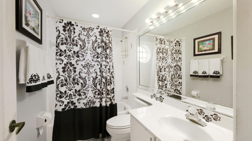 Modern bathroom with white fixtures and patterned shower curtain.