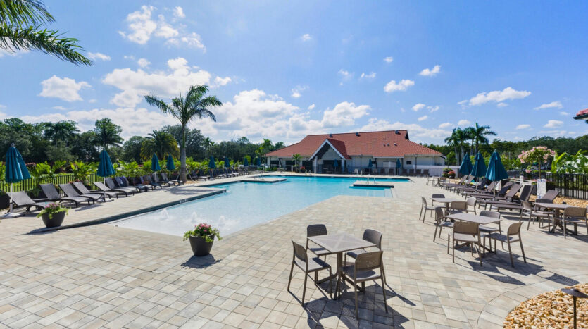 Sunny day at a spacious outdoor pool with lounge chairs and palm trees.