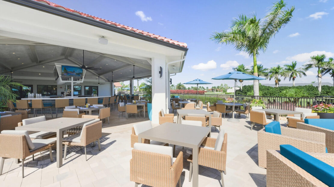 Outdoor patio dining area with wicker chairs and umbrellas under a clear blue sky.