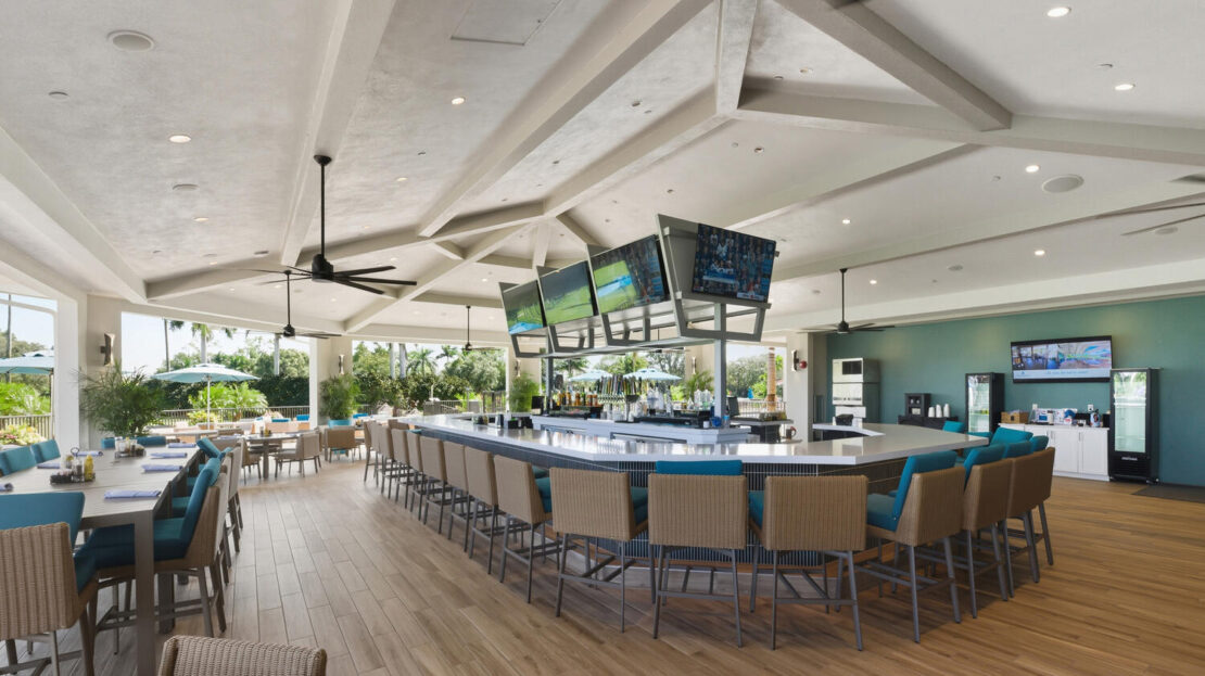 Modern bar with multiple screens and blue cushioned stools.