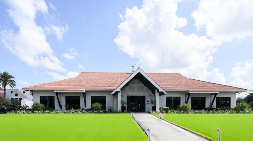 A modern building with a red roof and green lawn under a blue sky.