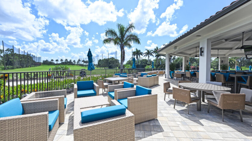 Sunny outdoor lounge with wicker furniture and palm trees under a bright blue sky.